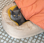 A cat laying under peach leaf-shaped blanket.