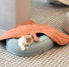 A cat sleeping under orange leaf-shaped blanket.