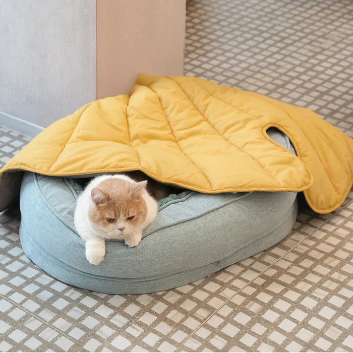 A cat sleeping under yellow leaf-shaped dog blanket mat