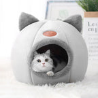 A white and gray cozy cat cave with a cat peeking out from the opening.