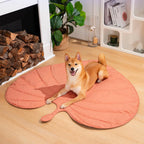A dog sitting on a peach leaf-shaped dog blanket mat.