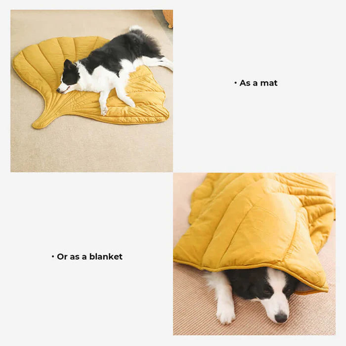A dog lying on a yellow leaf-shaped dog blanket mat on a wooden floor.