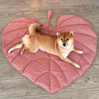 A dog lying on a pink leaf-shaped dog blanket mat on a wooden floor.
